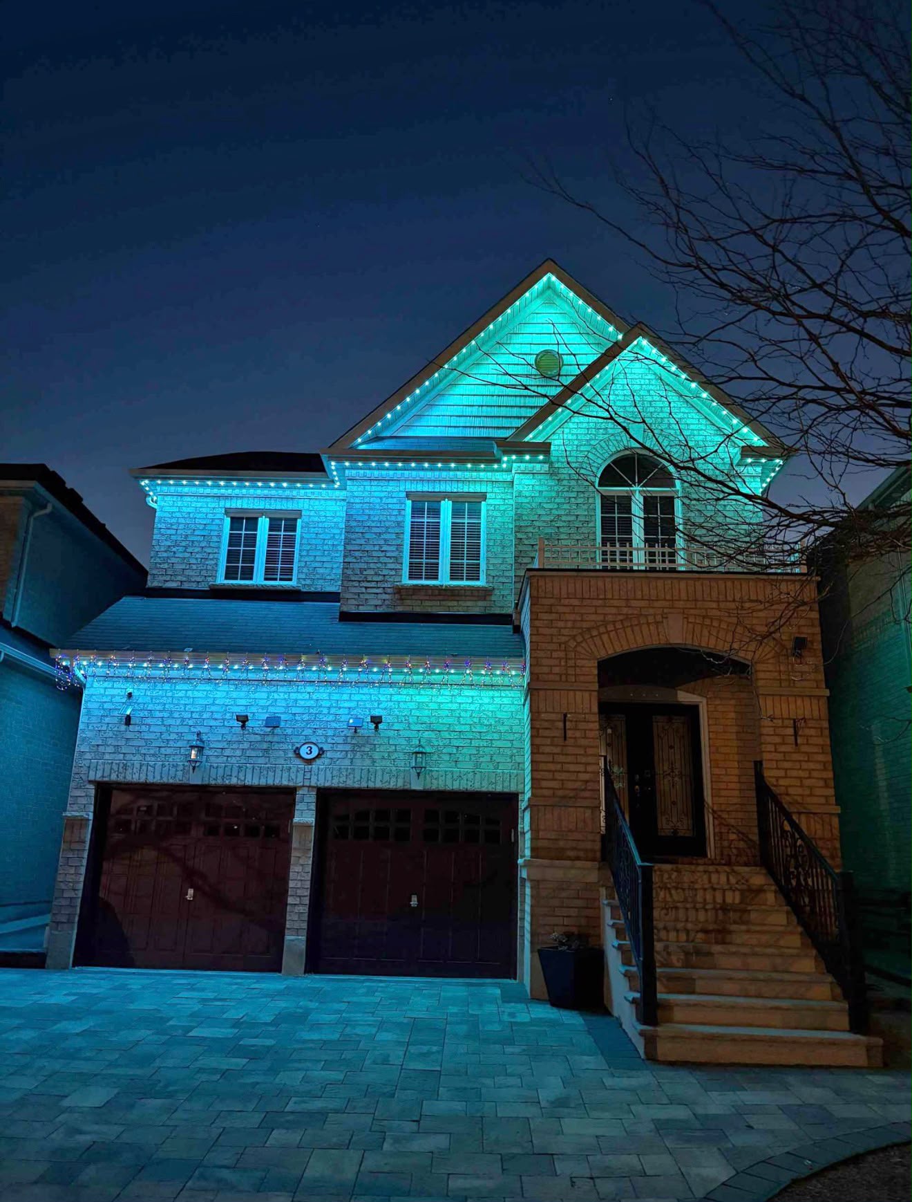 Two-storey brick home washed in cyan light along the rooflines and gables at night