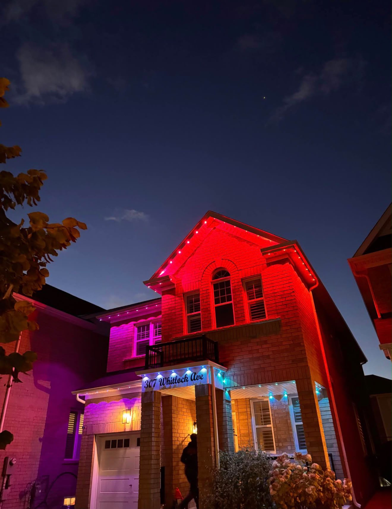 Brick home at night glowing red along the upper gables with purple light on the lower roofline